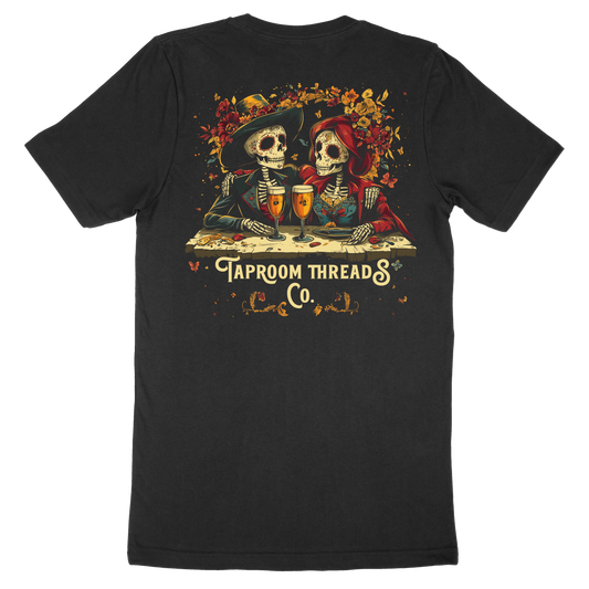 A black t-shirt with a graphic design featuring two skeleton figures, flowers, and the text 'TAPROOM THREADS CO.'